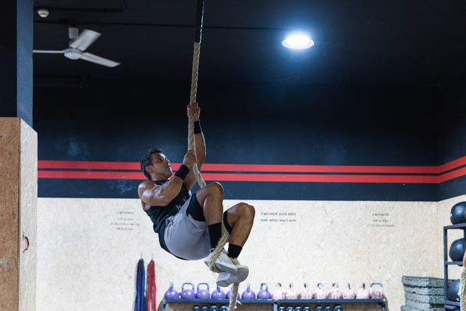 Strong sportsman exercising on climbing rope
