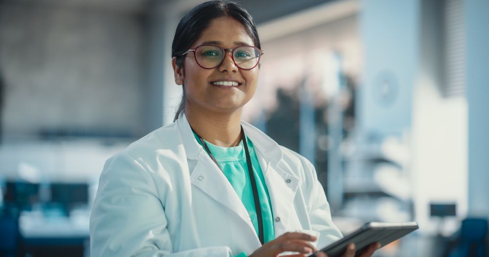 Portrait of Indian Young Female Scientist Using Digital Tablet Computer, Looking at Camera and Smiling in a Laboratory.