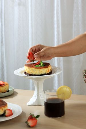Female Hnad Putting Strawberry on top of Basque Burnt Cheese Cake