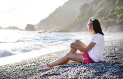 Young woman sitting on pebble beach looking into distance