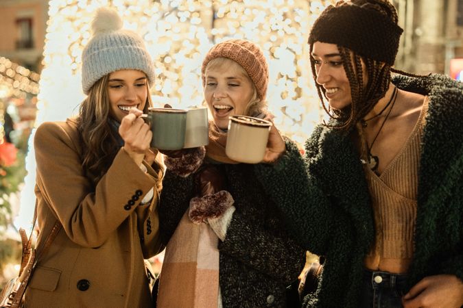 Three happy friends drinking a hot beverage and toasting at a Christmas market.