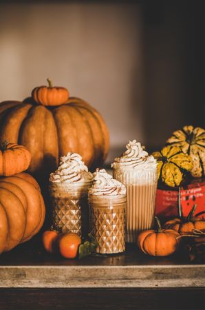 Three frothy drinks with whipped cream topping one table among decorative squashes, copy space