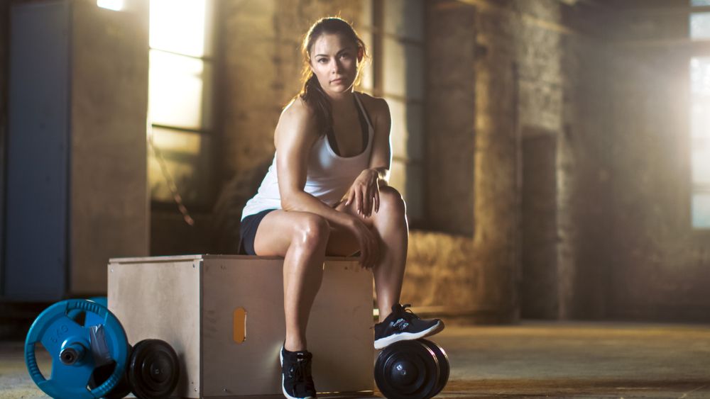 Athletic Woman Uses Smartphone For Tracking Her Intensive Cross Fitness Bodybuilding Exercise Program at Her Favourite Gym.