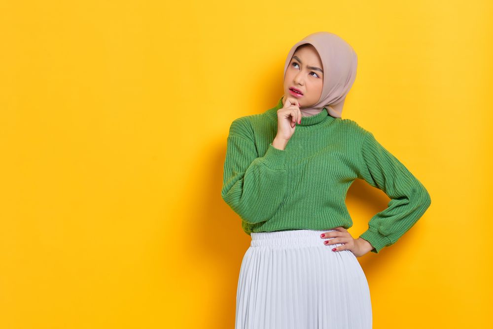 Woman in headscarf thinking about something with hand on chin with copy space
