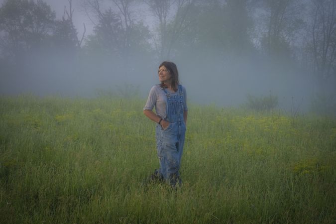Woman shepherd standing n a grass field in the fog