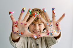 Positive kid showing hands with colorful confetti during party