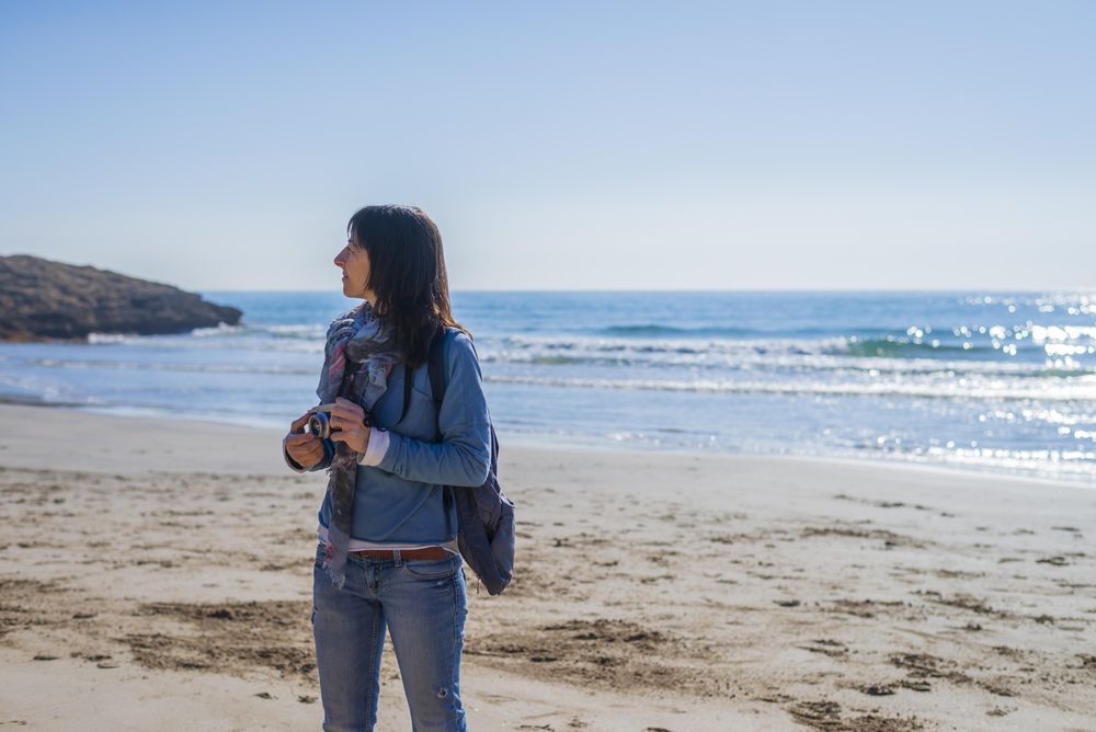 Female dressed in blue standing on the beach with camera