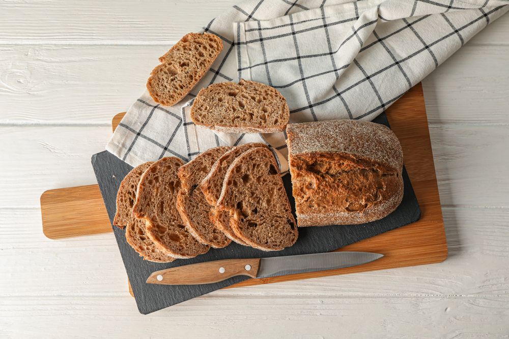 Composition with bread, knife, kitchen towel and cutting board on wooden background, top view and space for text