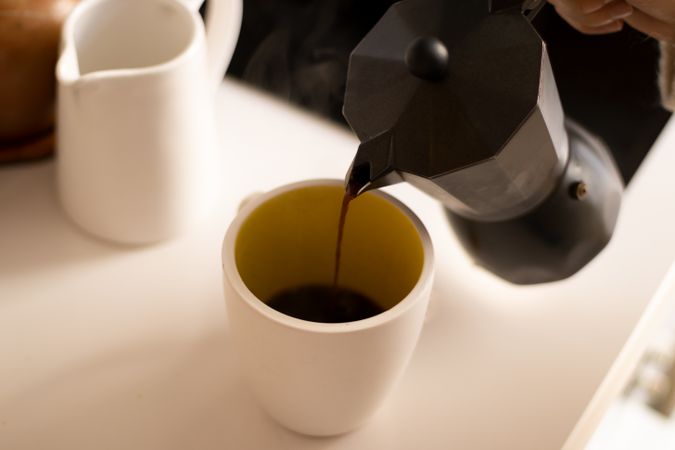 Pouring coffee on a cup in a kitchen.