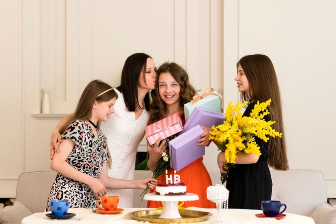 Friends celebrating birthday with cake, gifts, and flowers.