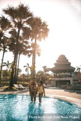 Man and woman standing in swimming pool near palm tree 0yMLO0