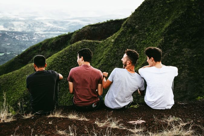 Back view of four young men sitting against mountainous landform