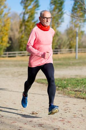 Grey haired man in red shirt and glasses exercising outside on fall day
