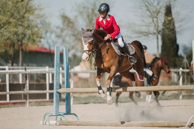 Teen girl riding horse and jumping over bars