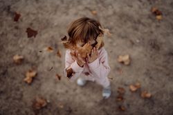 Joyful child scattering leaves on lawn in park