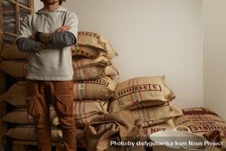 Tattooed barista stands proudly in front of big bags with imported raw coffee beans 5QnrV4
