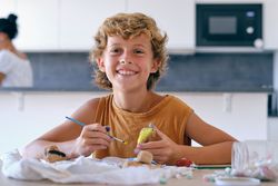 Cheerful boy painting stone at home