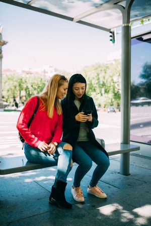 Female friends using smartphone on bus stop
