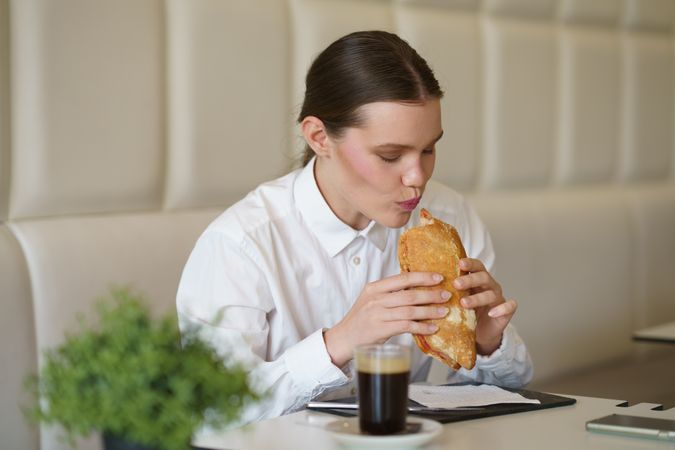 Starved businesswoman eating sandwich and drinking coffee in a cafeteria