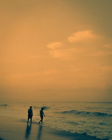 two men walking on beach during sunset