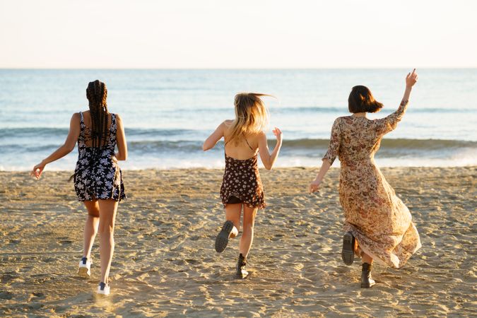 Backs of three happy women skipping towards the coast on beach