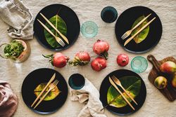 Fresh table setting on brown table cloth, leaves on dark plates, pomegranate