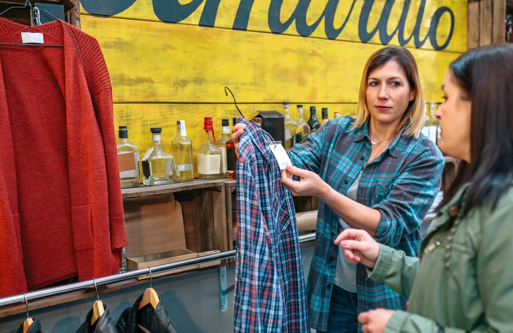 Woman shop assistant showing label price of plaid shirt to client in shop