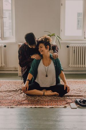 Man rubbing shoulders of joyful woman resting on floor at home