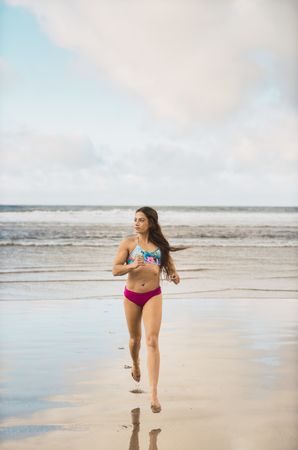Woman in swimwear running near sea