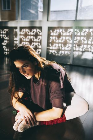 Young woman bending forward stretching legs while sitting on studio in sunlight.
