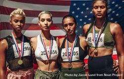Portrait of four female athletes with gold medals standing in front of USA flag 4BJMx4