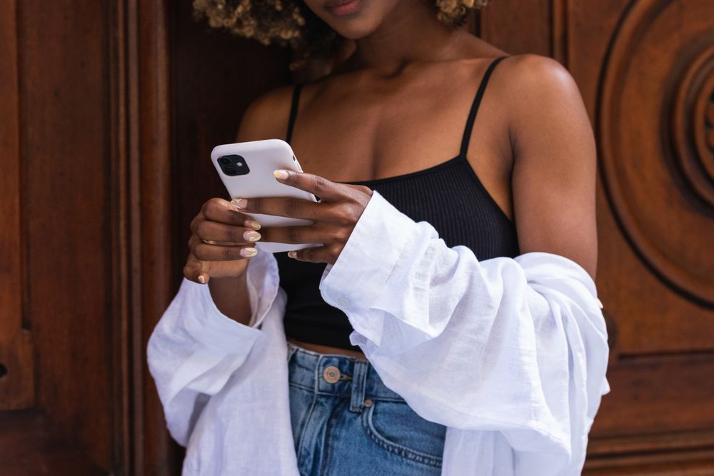 Anonymous Black woman browsing smartphone near old gates old wooden door