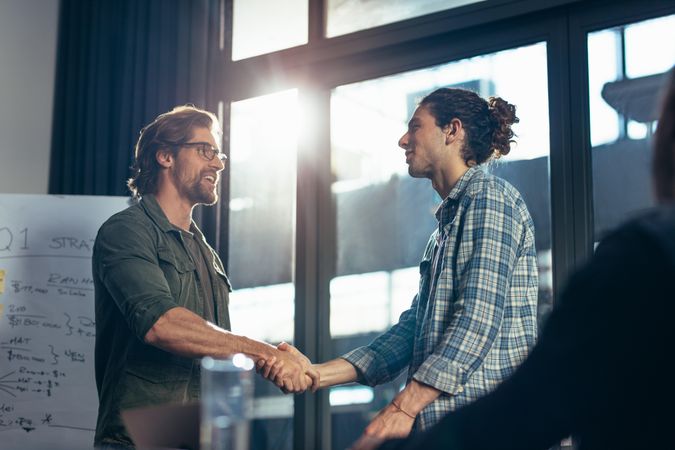 Young businessman shaking hands with male colleague after meeting in boardroom
