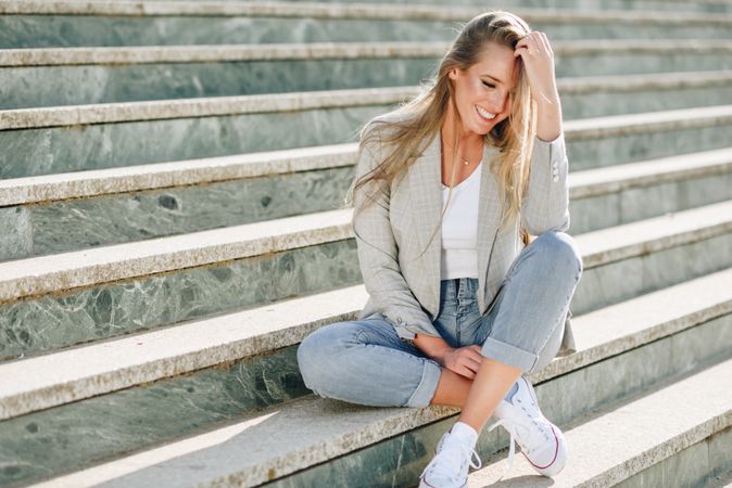 Joyful woman in blazer sitting on outdoor steps on sunny day