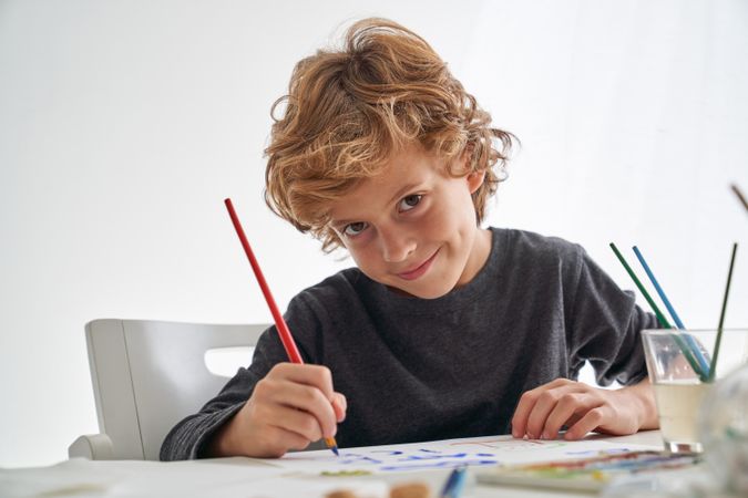 Cheerful boy painting at table