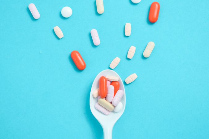 Plastic spoon with various colorful pills on blue table with space for text