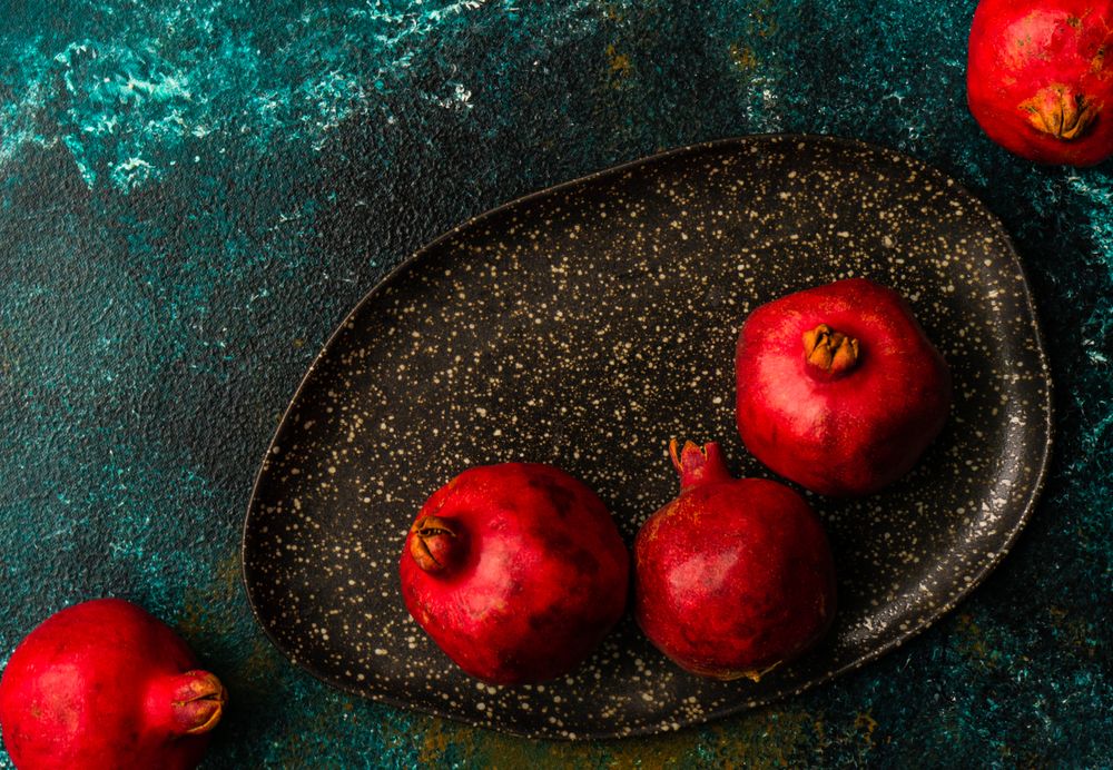 Whole pomegranates on dark ceramic plate on green surface