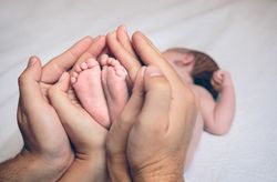 Parents hands holding feet of newborn lying over bed