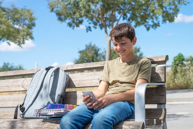 Smiling teenage boy looking at phone on bench