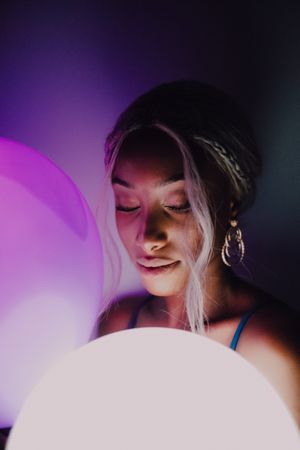 Black adult woman with illuminated balloon in darkness looking at camera