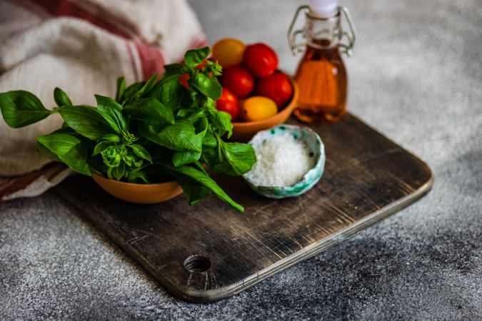 Fresh basil, cherry tomatoes, salt and oil on bread board