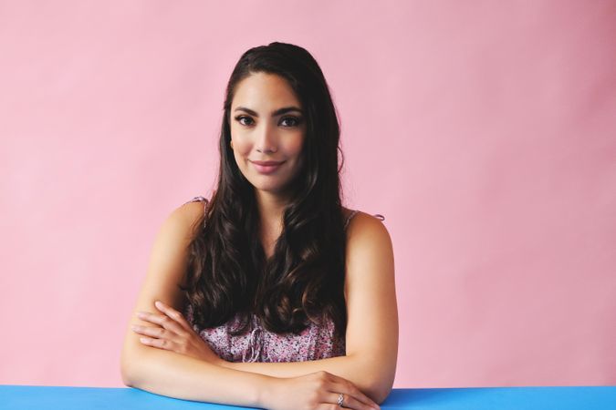 Hispanic woman sitting at blue table in pink room