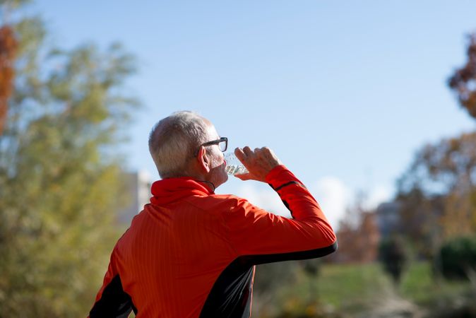 Back of older man sipping from water bottle in park