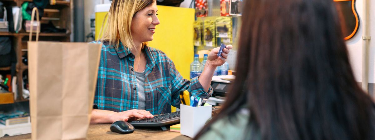Banner of woman shop assistant registering client data in store terminal to make invoice of purchase