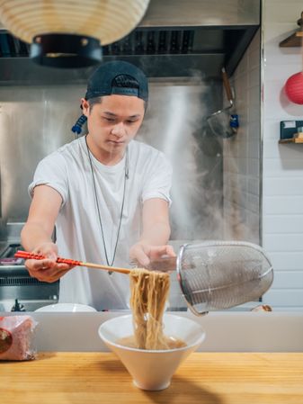 Asian male cooking ramen in cafe
