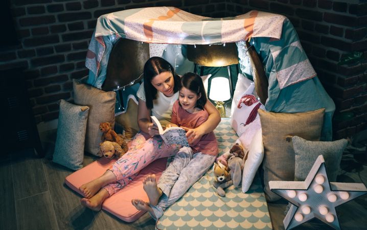Mother and daughter reading a book in a diy tent