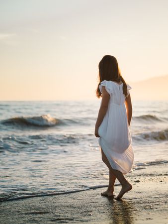 Adorable girl walking on seaside at sunset