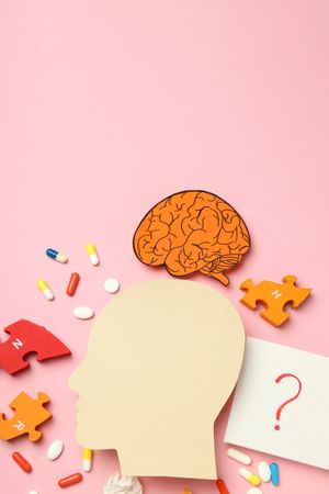 Paper cut out of side view of head with medications and puzzle pieces, vertical with copy space