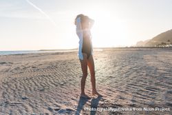 Woman with her arms up on beach at sunset in oversized shirt bYRJd0