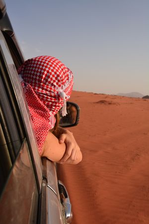 Person wearing red keffiyeh in car in desert